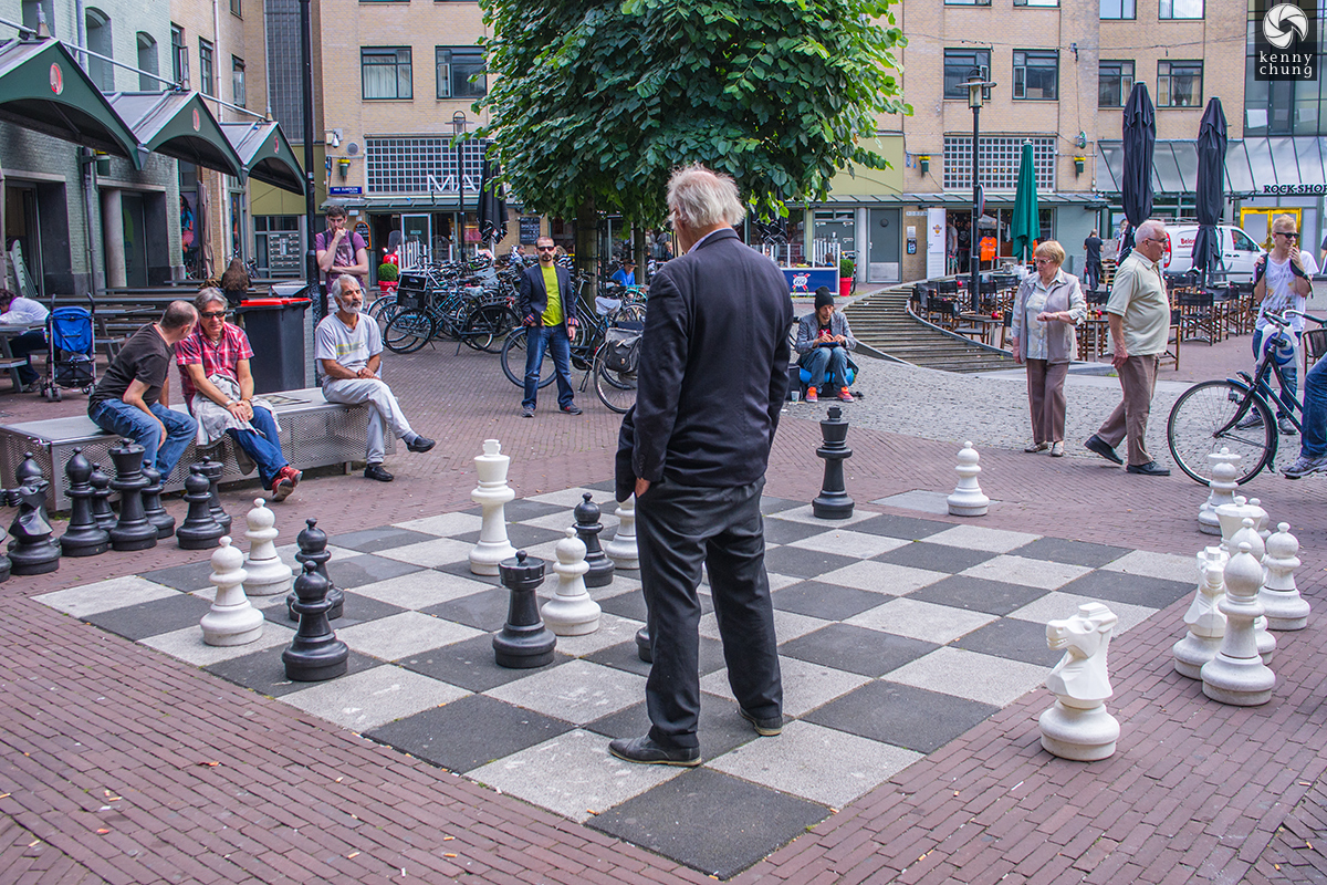 An older gentleman playing life size chess in a plaza in Amsterdam