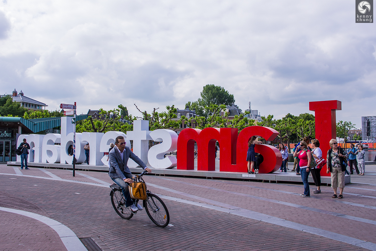 A man riding his bicycle behind the I Am Amsterdam sign