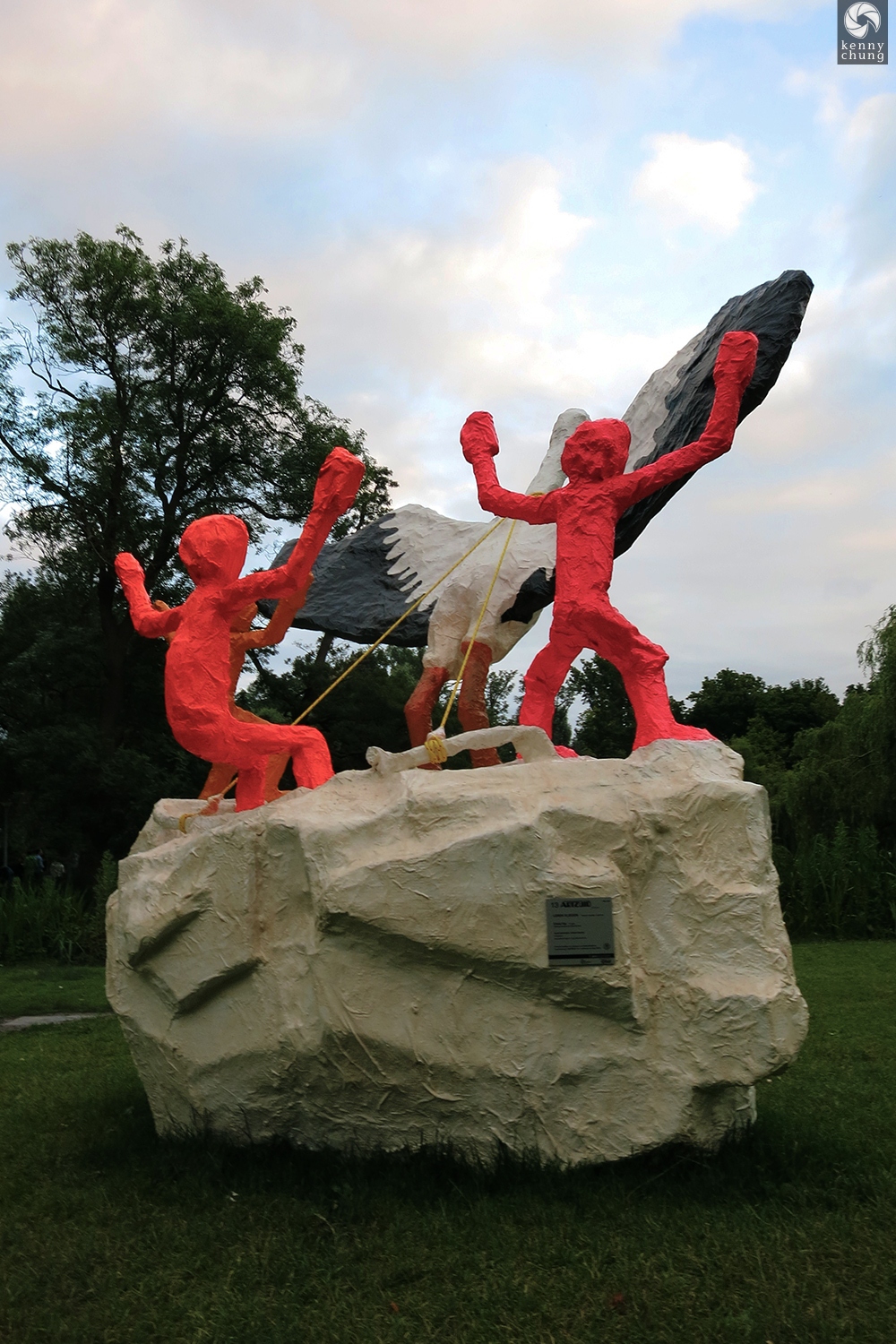 A sculpture of two red people dancing with a bird on a rock in Vondelpark