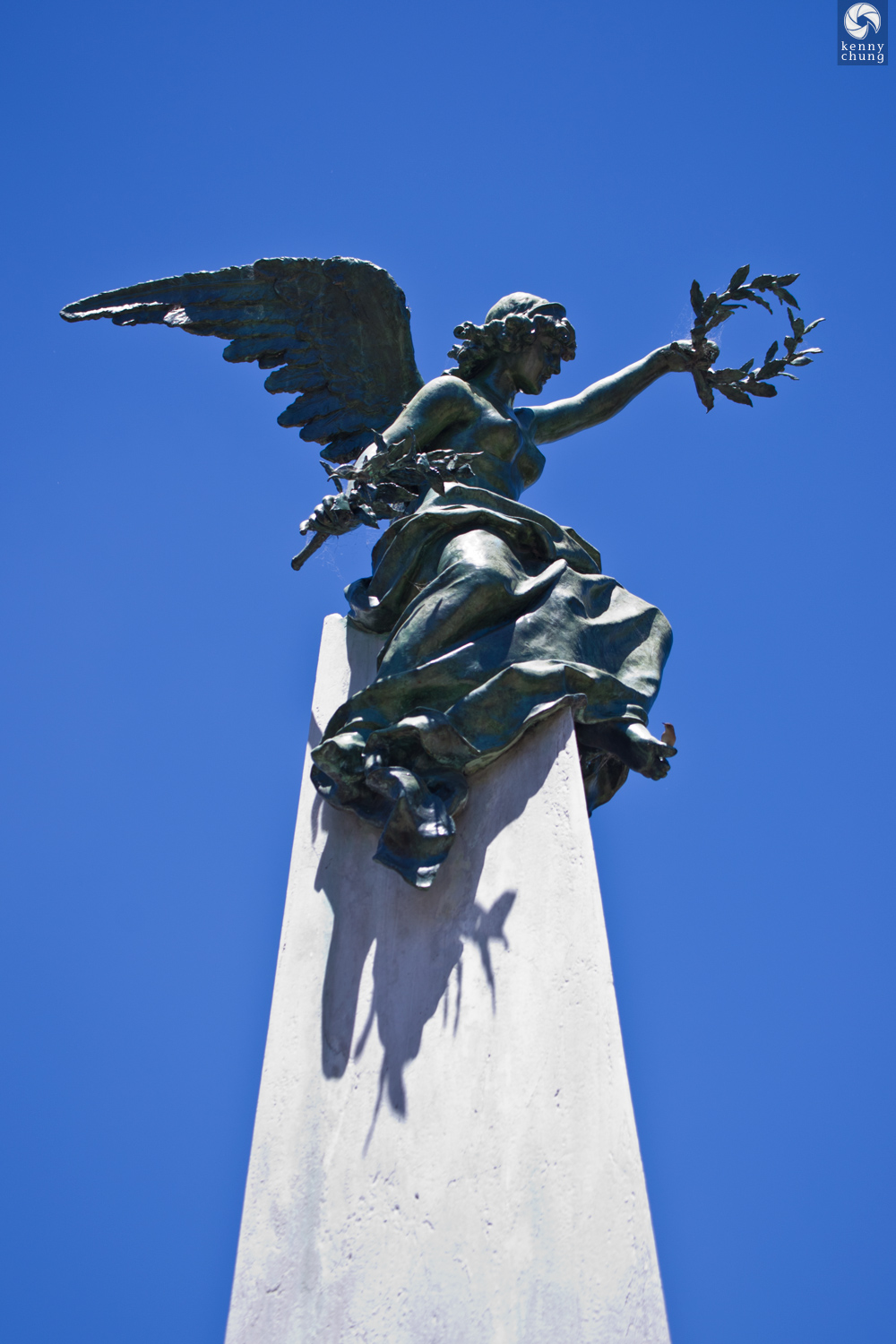 A statue of a seated angel holding olive brances at La Recoleta cemetery.